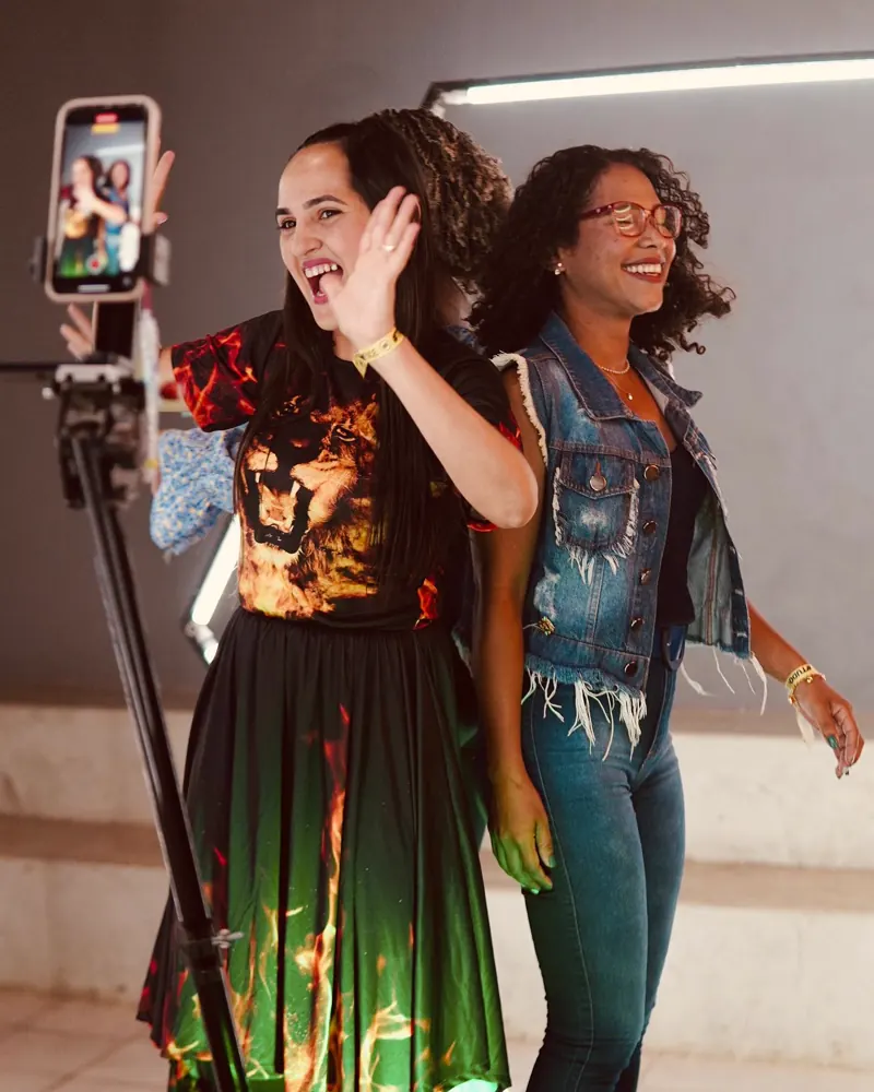 Amigas sorrindo e acenando durante a gravação na Plataforma 360
