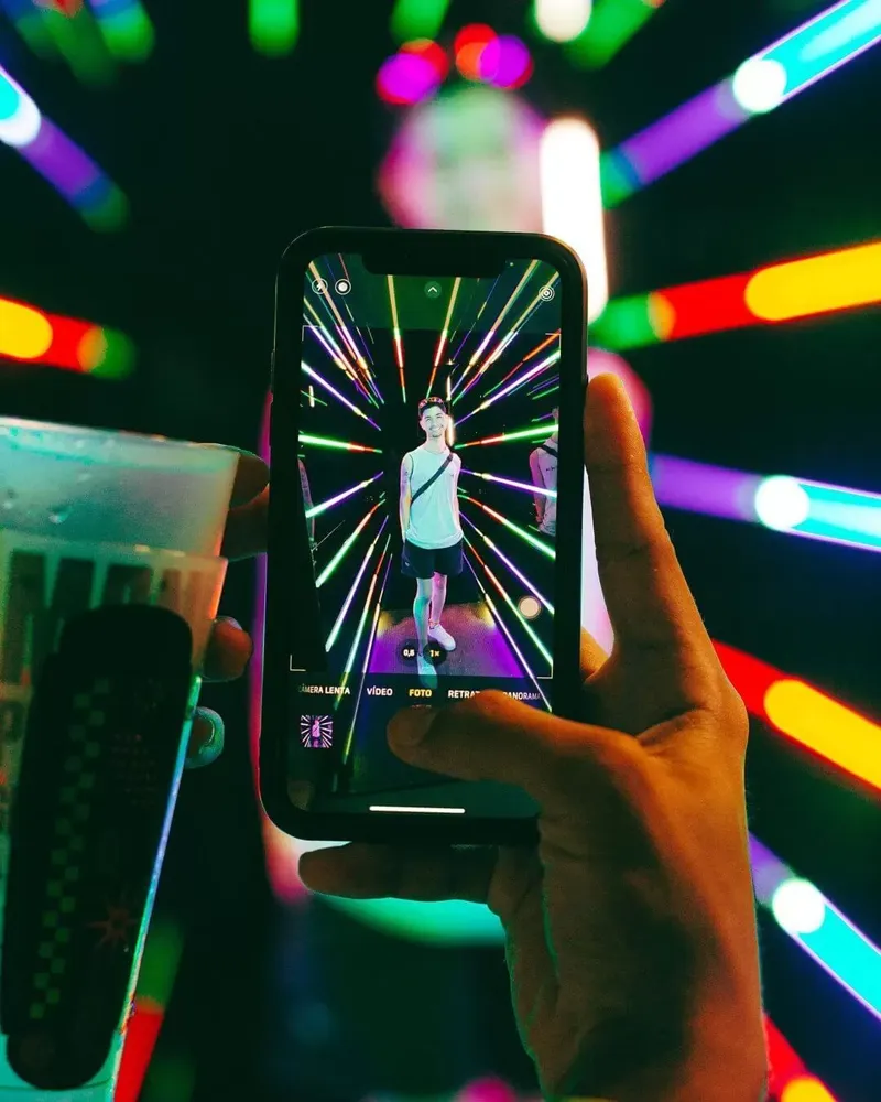 Convidado sendo fotografado com o celular dentro do Túnel Infinity, cercado de LEDs coloridos